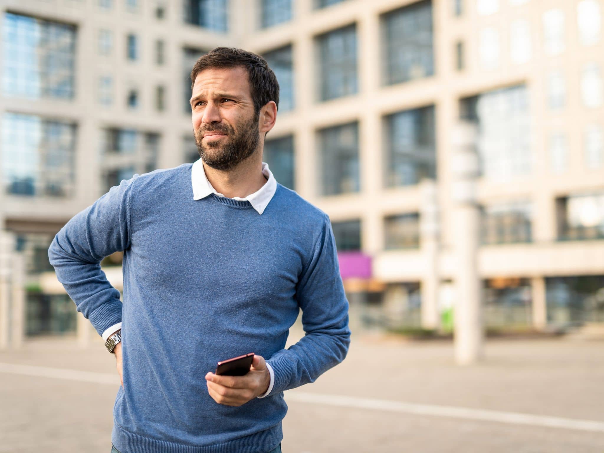 Ischiasschmerzen: Mann mittleren Alters steht auf der Straße und hält sich den unteren Rücken vor Schmerzen.