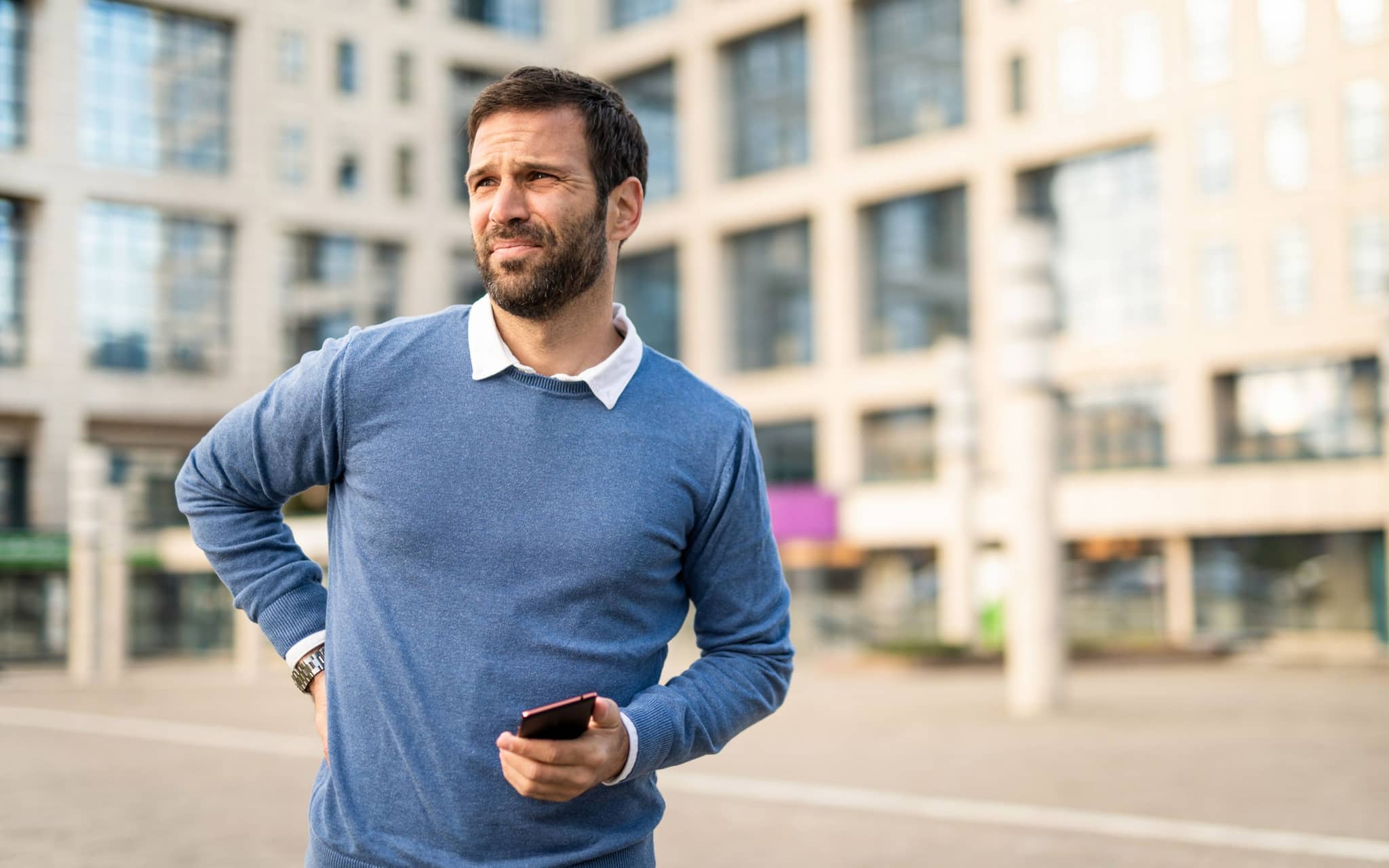Ischiasschmerzen: Mann mittleren Alters steht auf der Straße und hält sich den unteren Rücken vor Schmerzen.