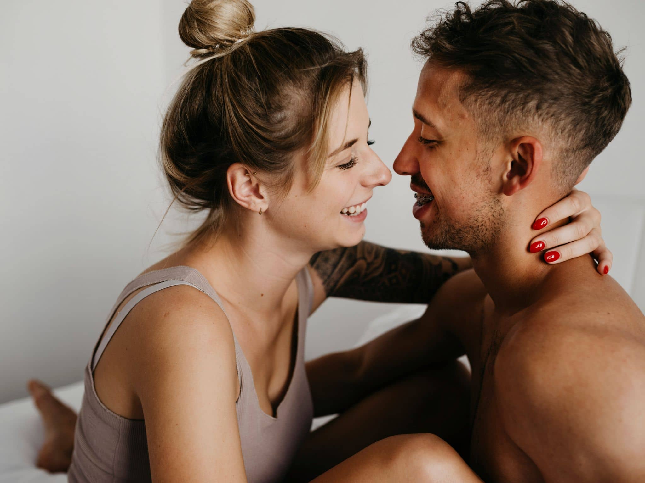 Blowjob: Eine junge Frau und ein junger Mann sitzen in Unterwäsche im Bett, lächeln sich an und umarmen sich.