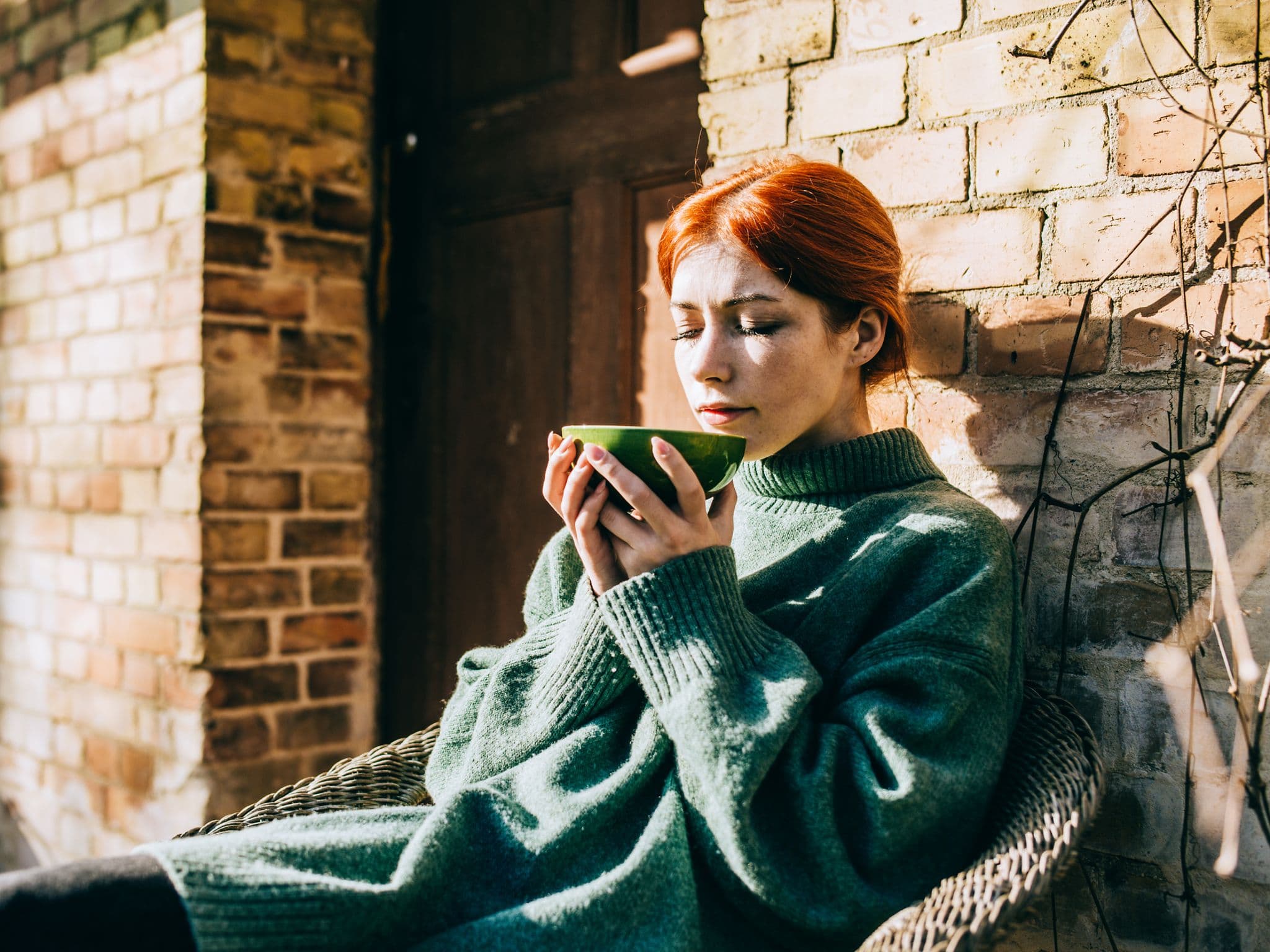 Richtig fasten: Junge Frau sitzt draußen vor der Haustür und trinkt eine Tasse Tee.