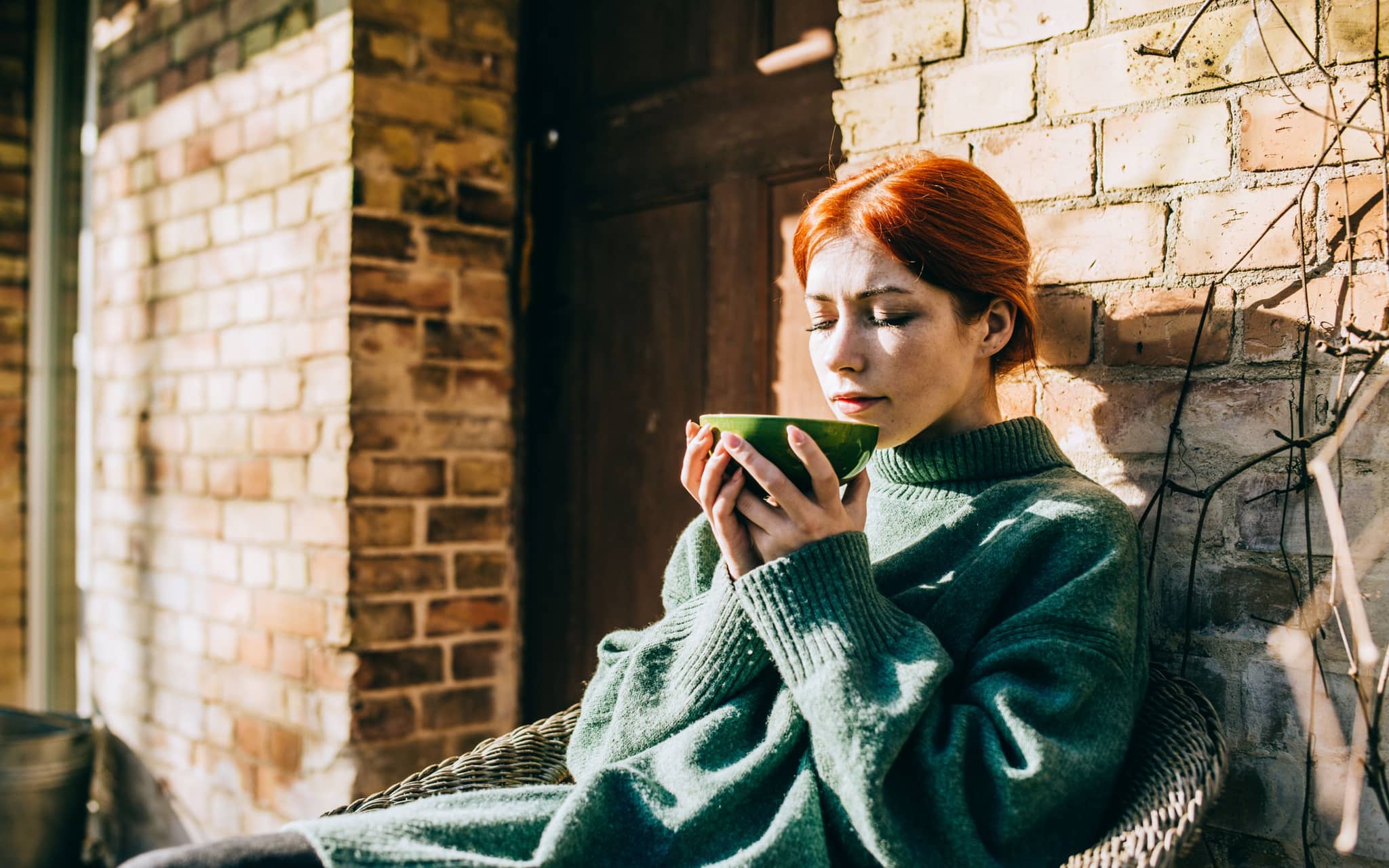 Richtig fasten: Junge Frau sitzt draußen vor der Haustür und trinkt eine Tasse Tee.
