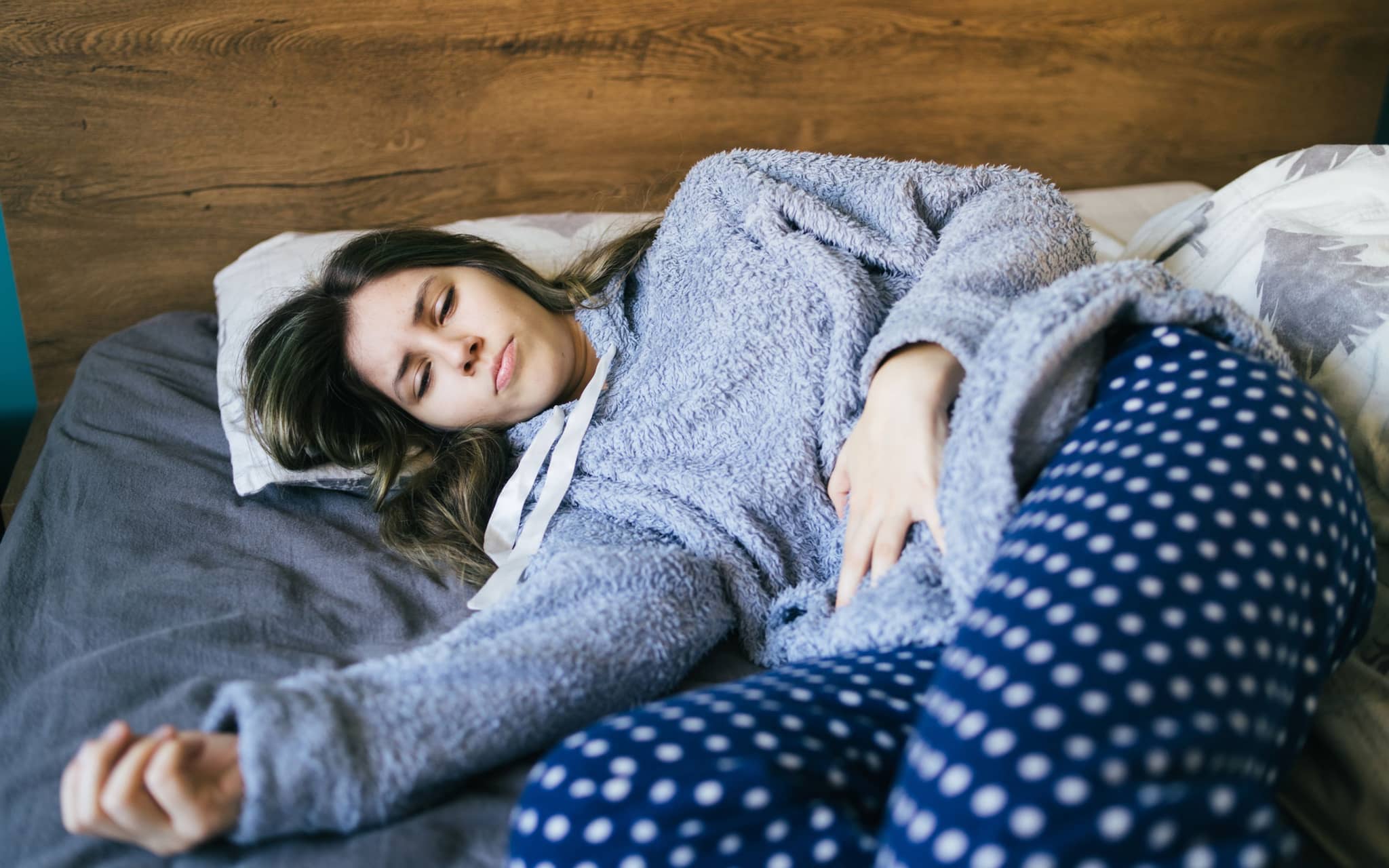 Lichen Sclerosus: Junge Frau liegt betrübt im BEtt und hält ihren Bauch fest.