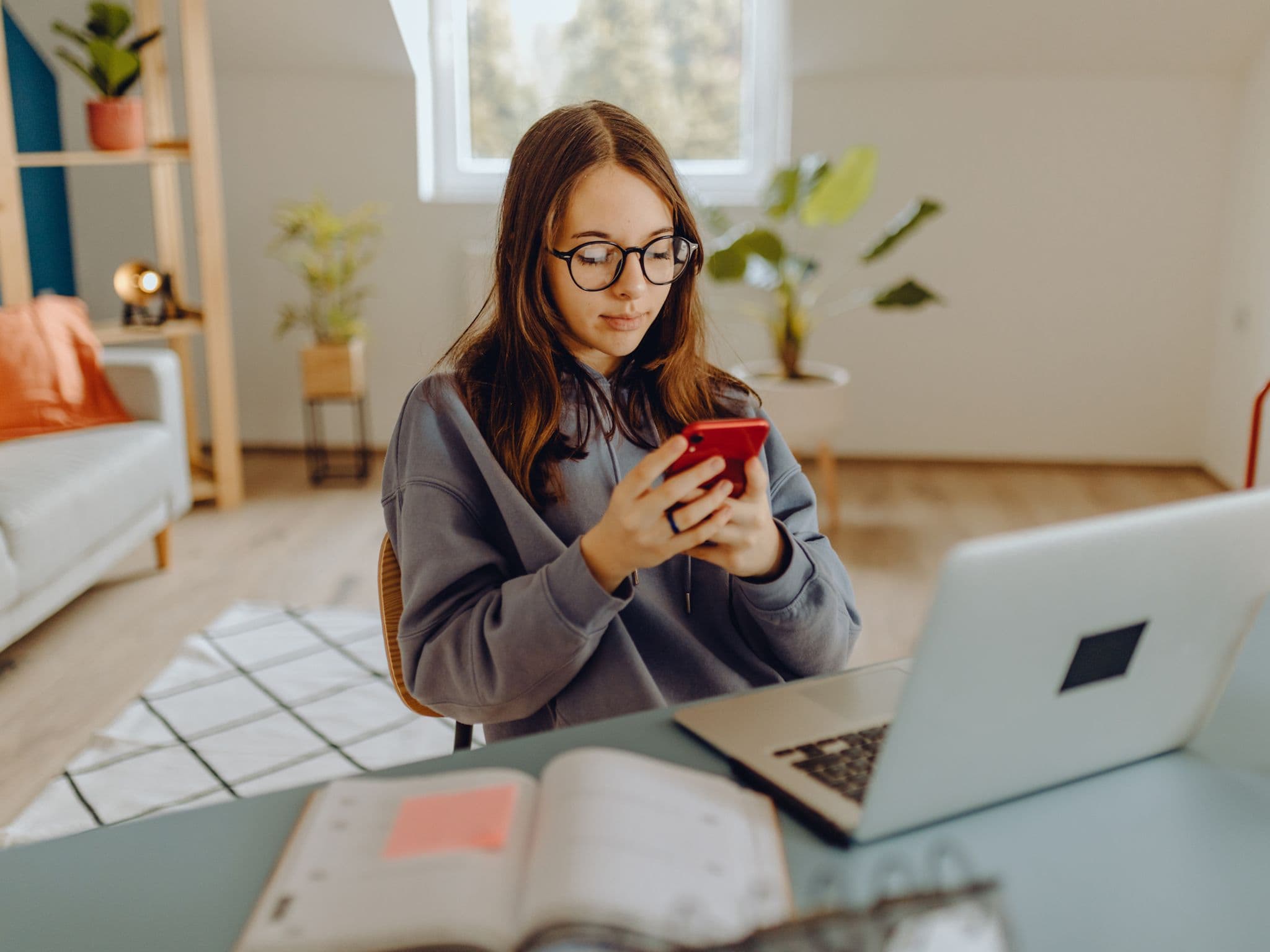 Image: Young woman sitting at her desk looking at her smartphone.