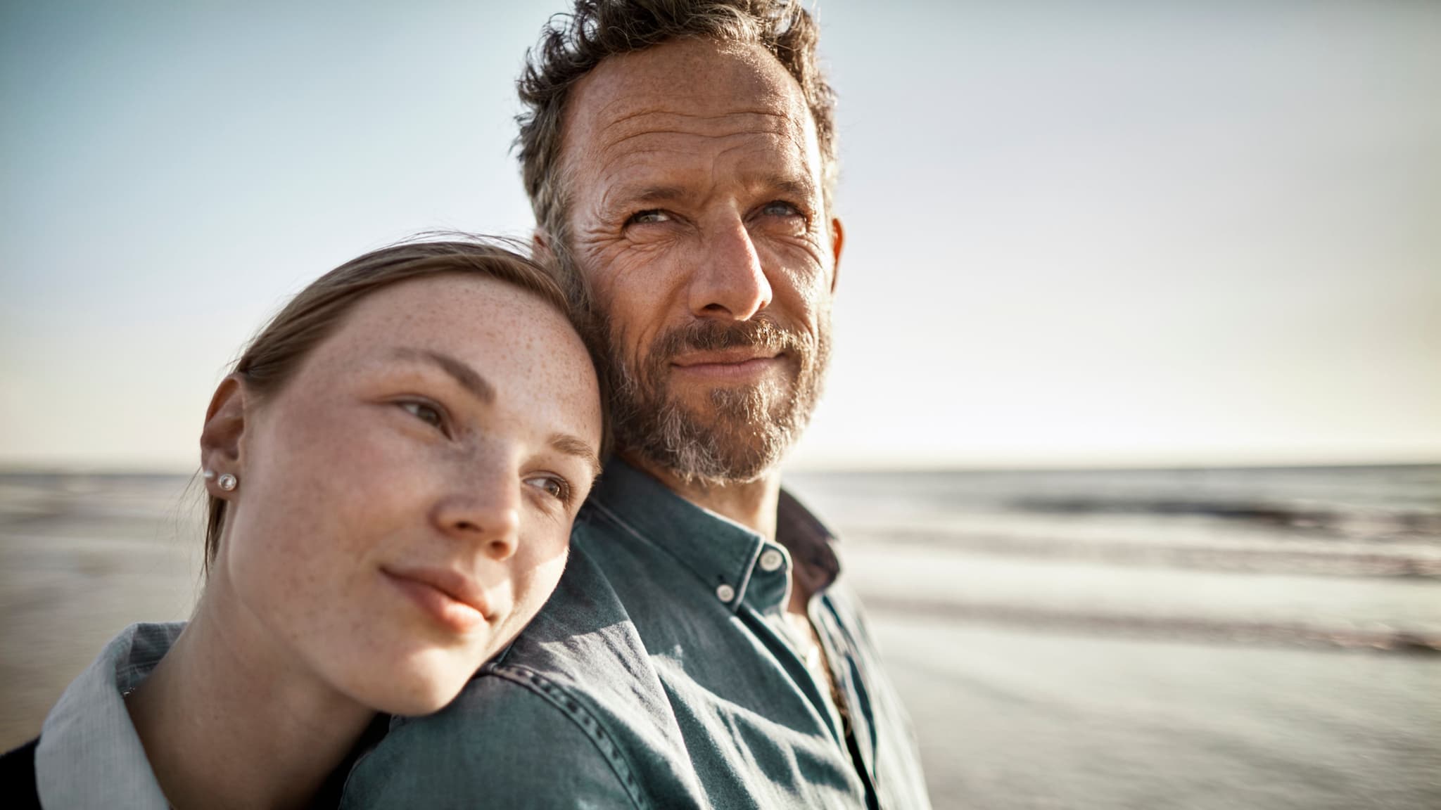 Suchtvermeidung: Junge Frau und mittelalter Mann blicken nachdenklich aufs Meer.