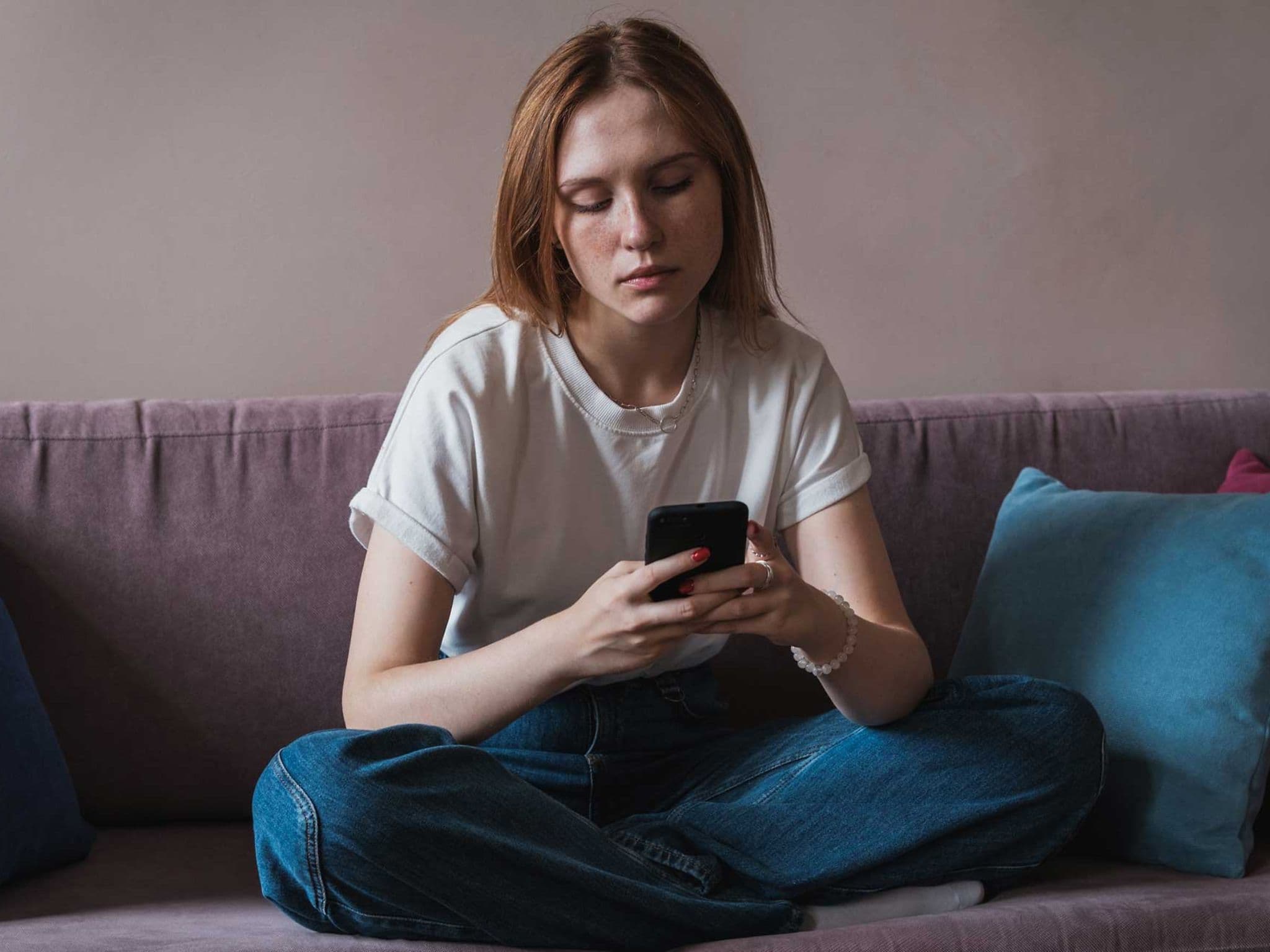 Doomscrolling: Junge Frau schaut niedergeschlagen auf ihr Handy