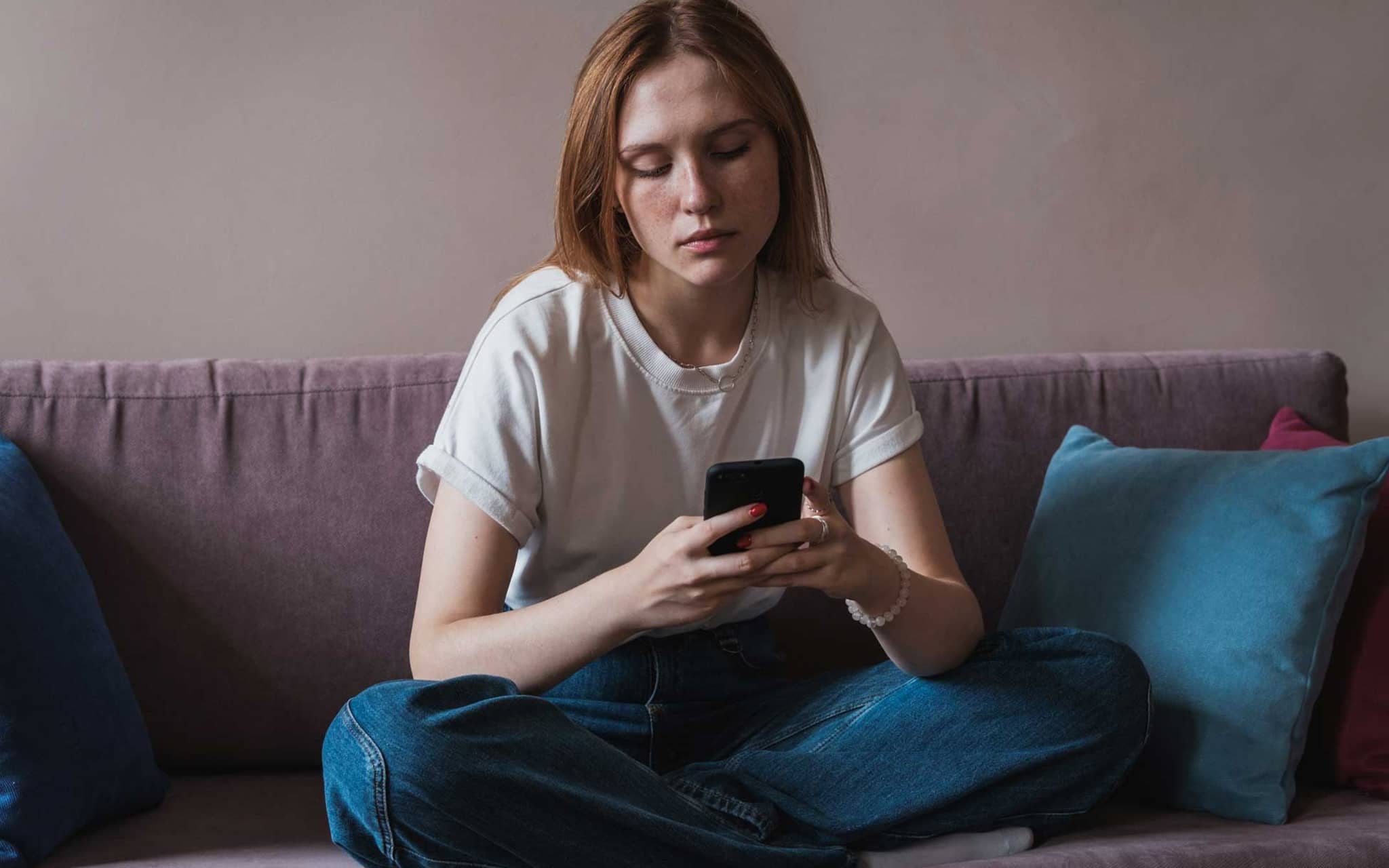 Doomscrolling: Junge Frau schaut niedergeschlagen auf ihr Handy