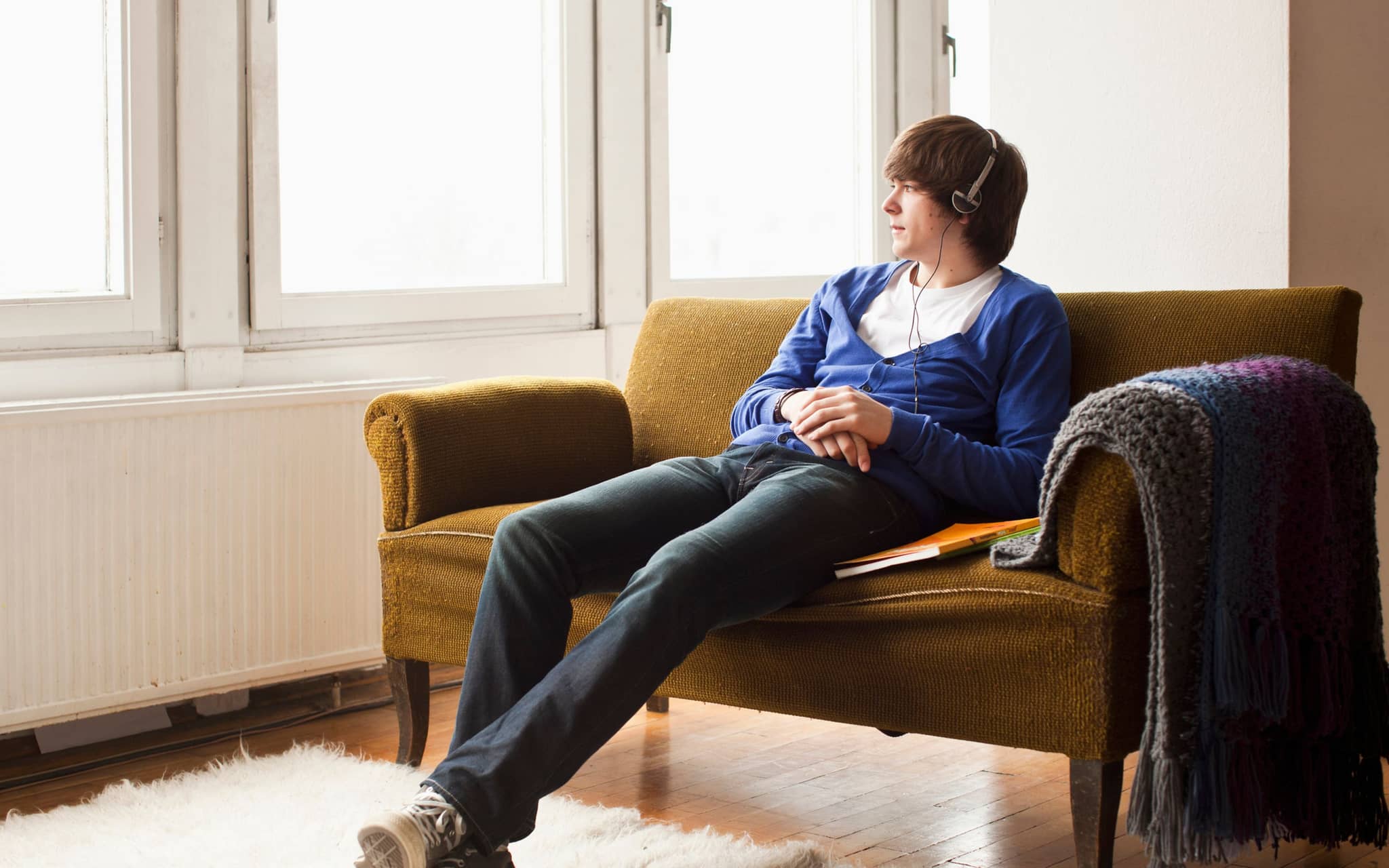 Symbolbild für Schmerzen am Penis: Ein junger Mann sitzt auf dem Sofa hört Musik und chillt