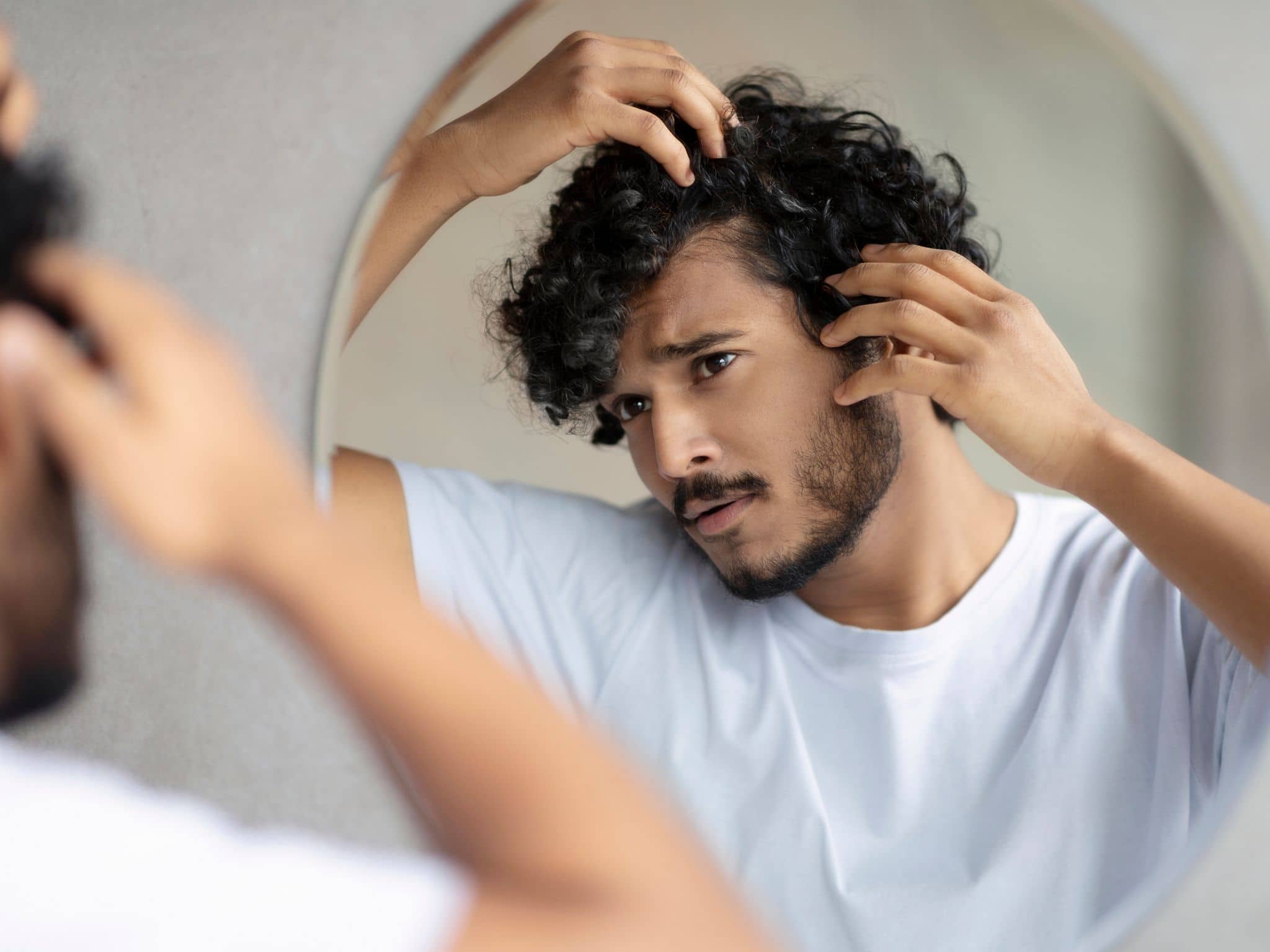 Haarausfall bei Männern: Ein junger Mann steht vor dem Spiegel und kontrolliert seine Geheimratsecken..