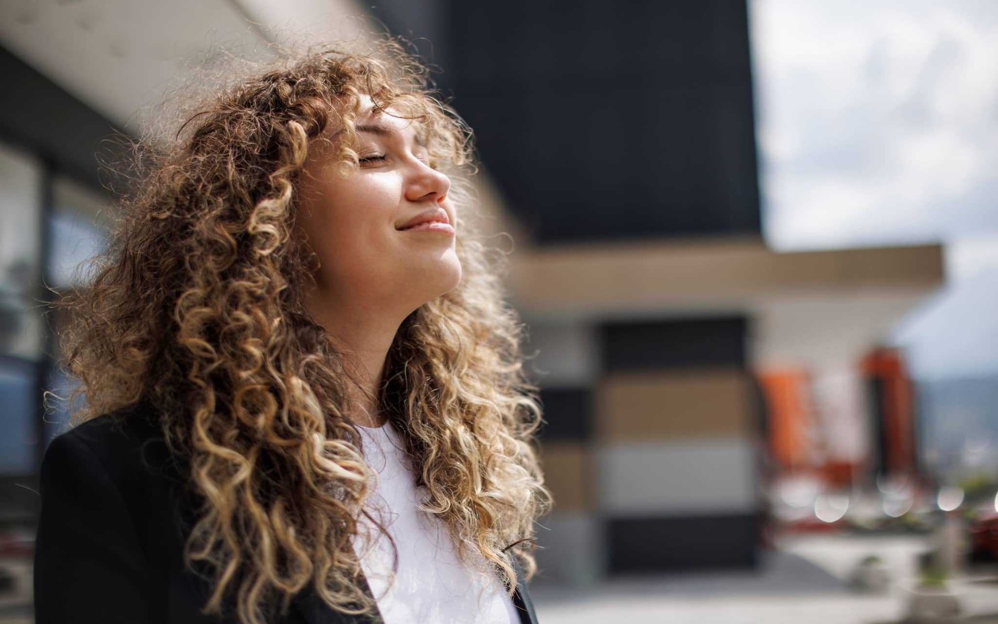 Picture: Young woman with curls enjoying the sun with her eyes closed.