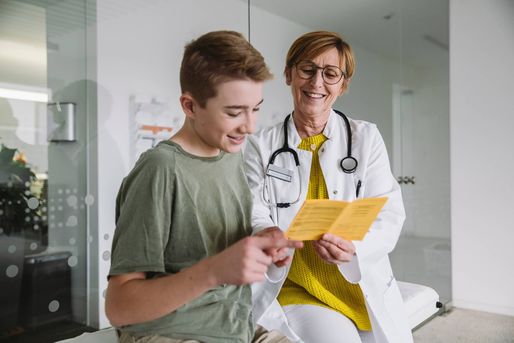 PaedCheck: Teenager schaut gemeinsam mit seiner Ärztin in sein PaedCheck-Heft
