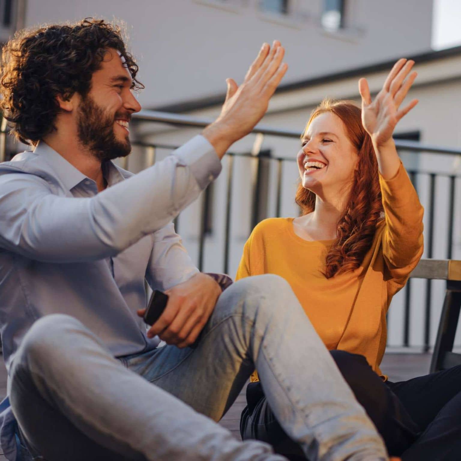 Beitragssatz 2024: Ein Mann und eine Frau sitzen vergnügt auf der Straße und klatschen sich mit den Händen ab.