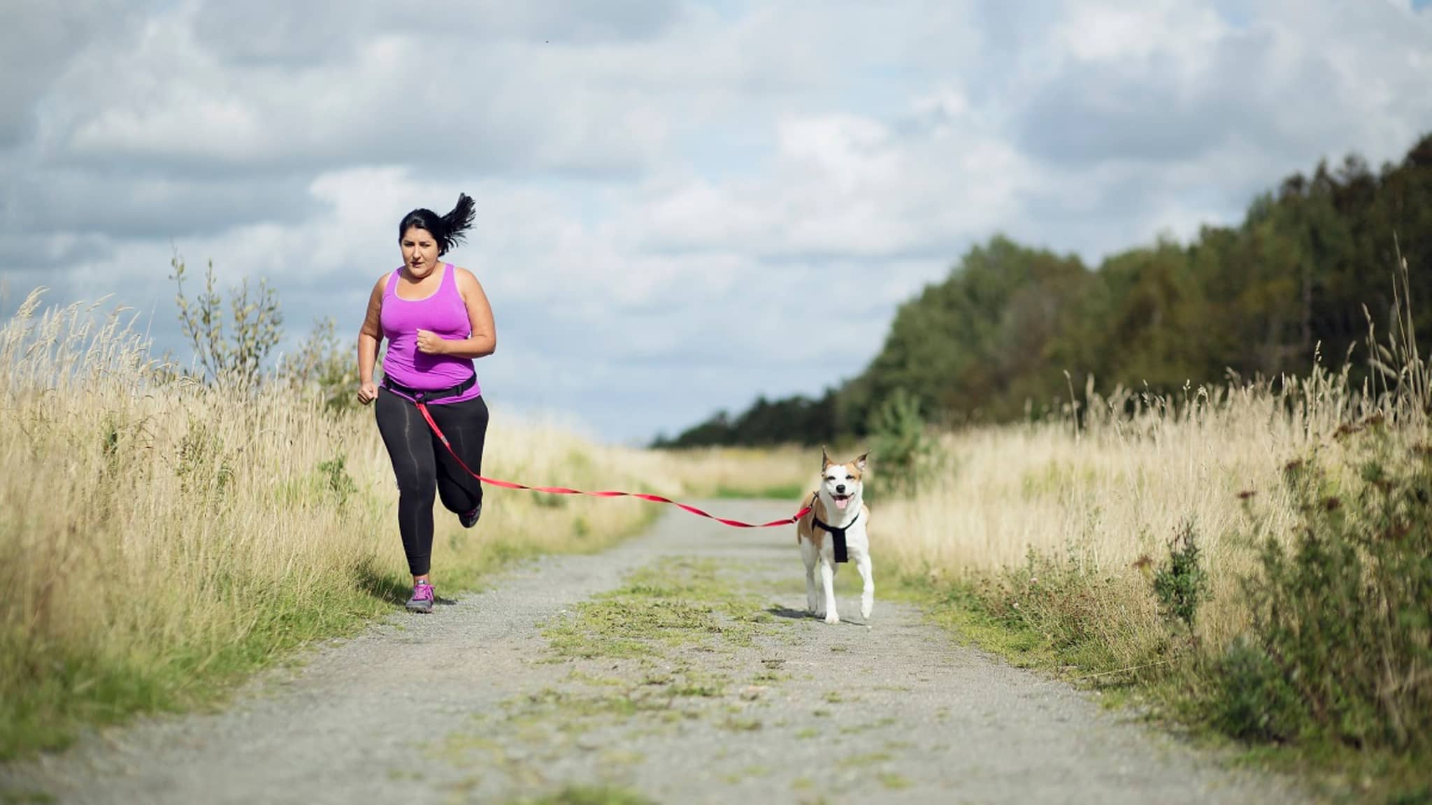 Bonusprogramm: Mollige Frau joggt mit ihrem Hund und sichert sich ihren DAK-Fitnesstracker.