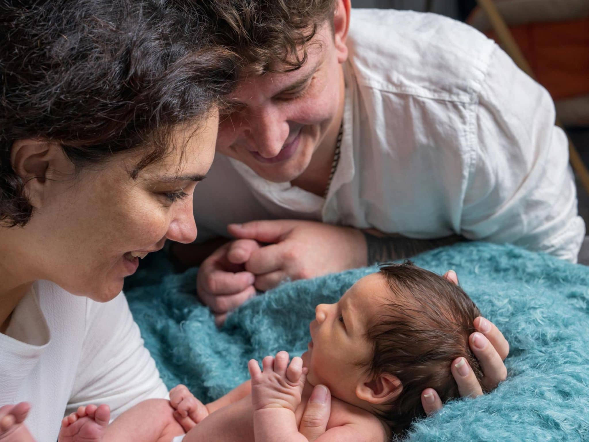 Geburtshilfe: Ein glückliches Paar schaut nach der Geburt zärtlich auf das Baby.