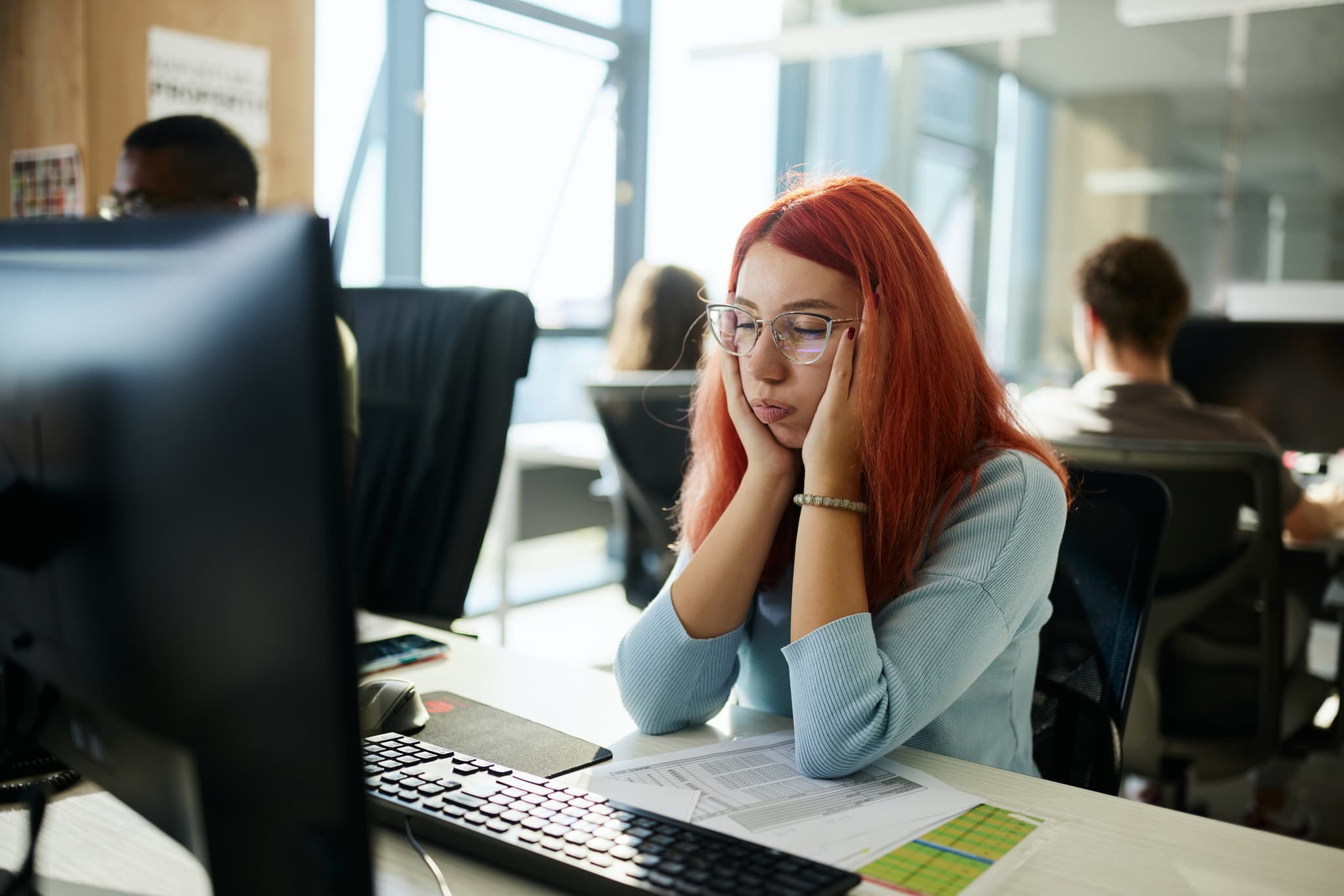 Frau ist gelangweilt bei der Arbeit am Schreibtisch und sucht Motivation
