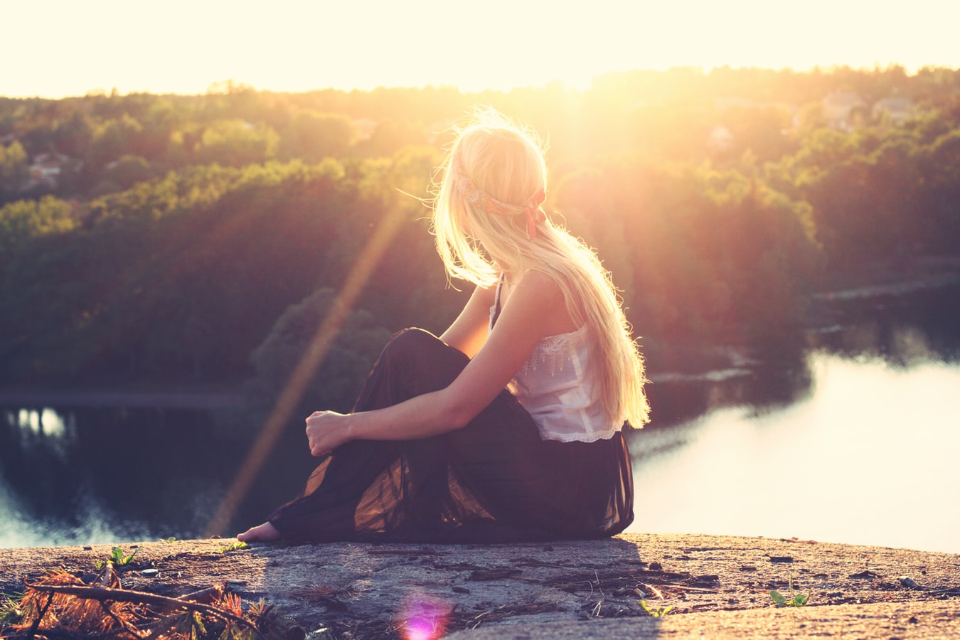 Eine Frau mit blonden Haaren sitzt auf einem Berg und genießt den weiten Blick
