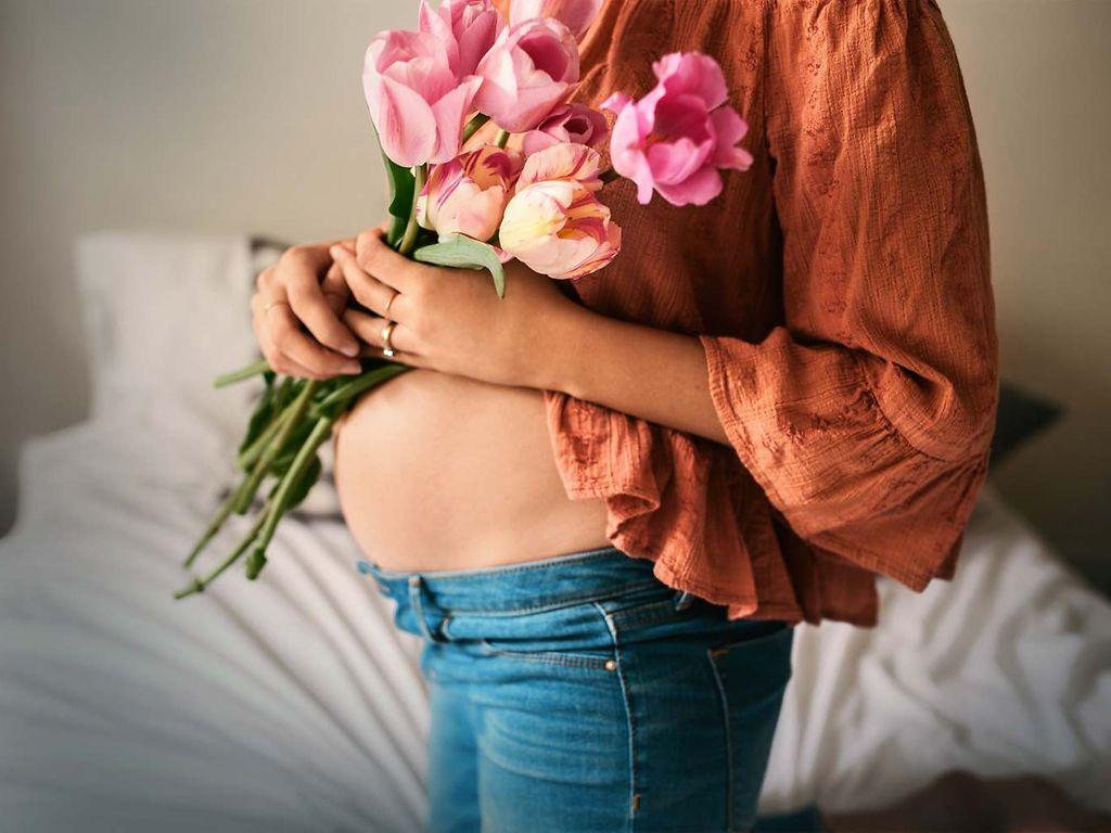 DAK MamaPLUS: Schwangere hält sich Blumen vor den nackten Bauch