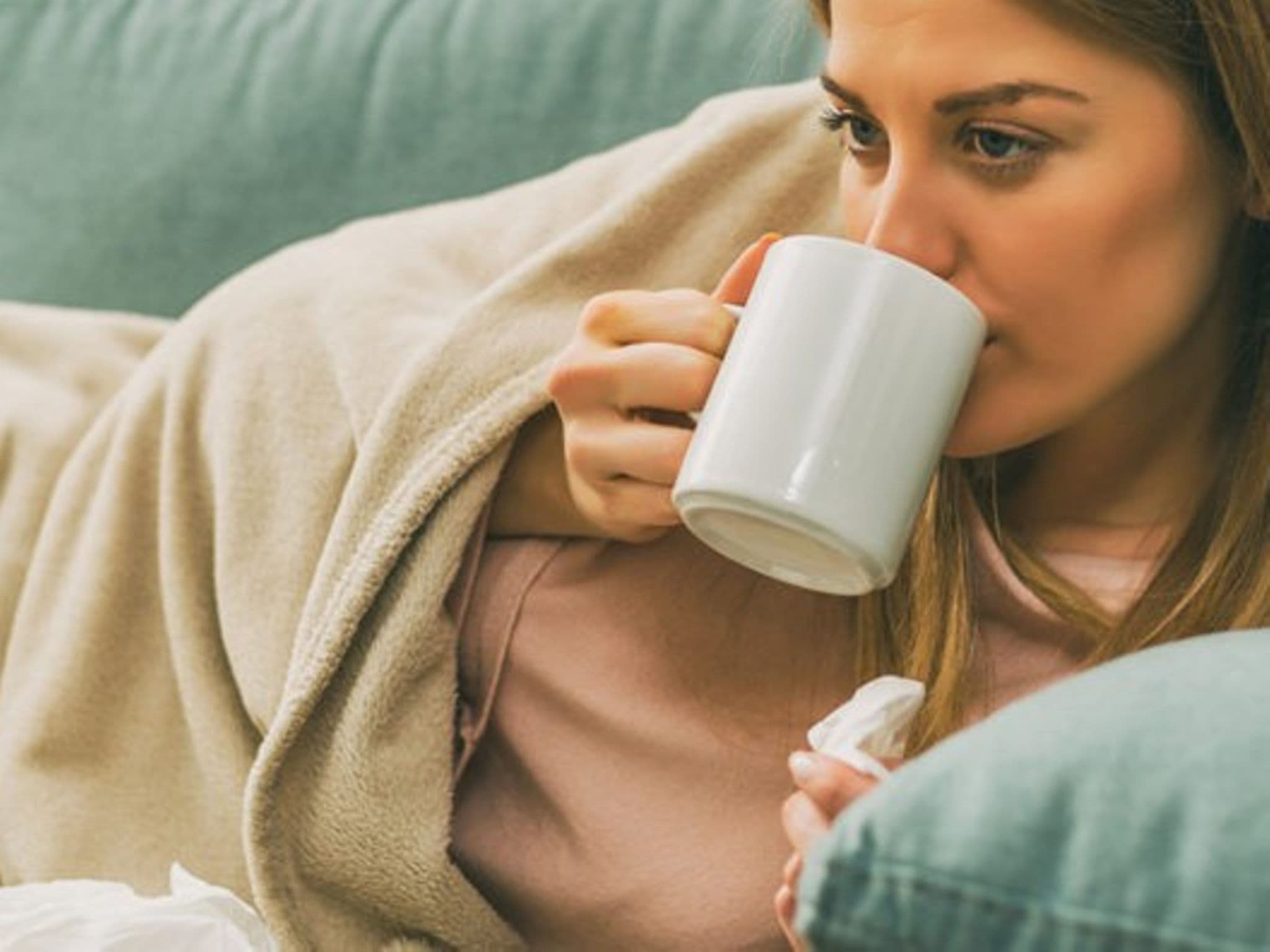 Erkältete Frau liegt auf dem Sofa und trinkt Tee