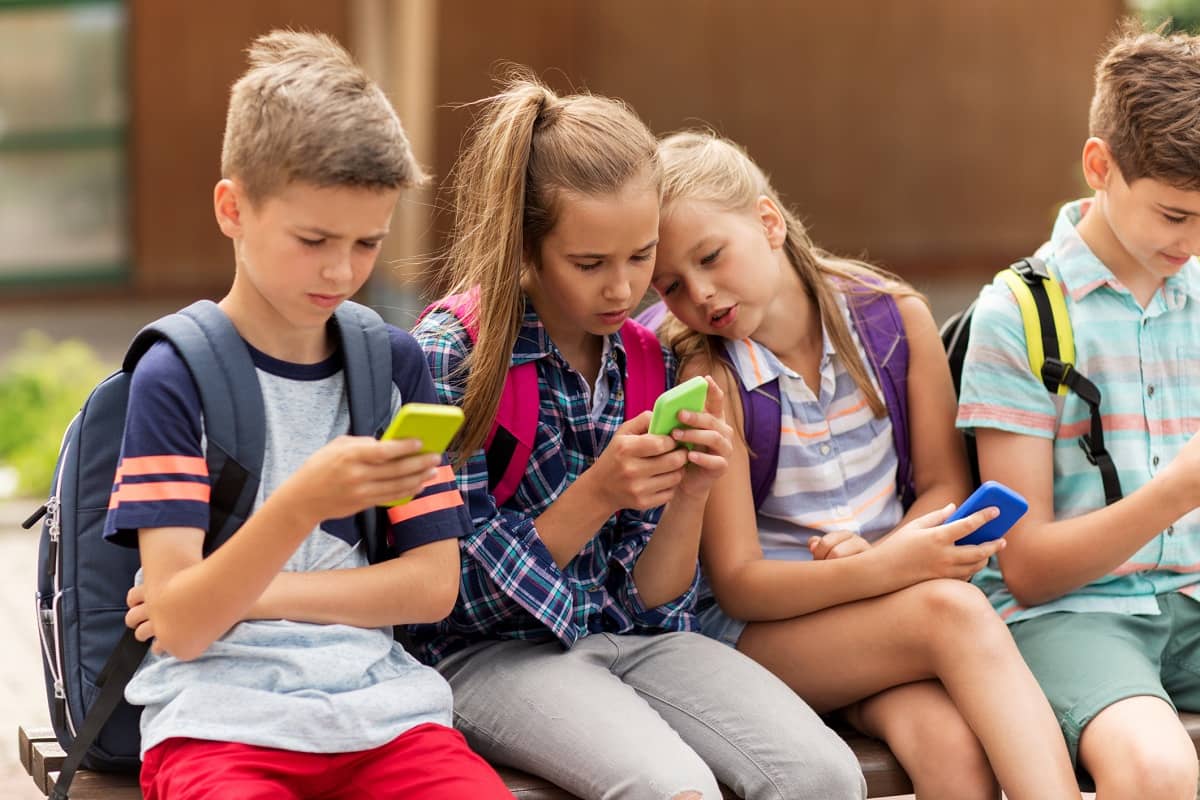 Vier Grundschulkinder auf dem Schulhof nutzen Smartphones.