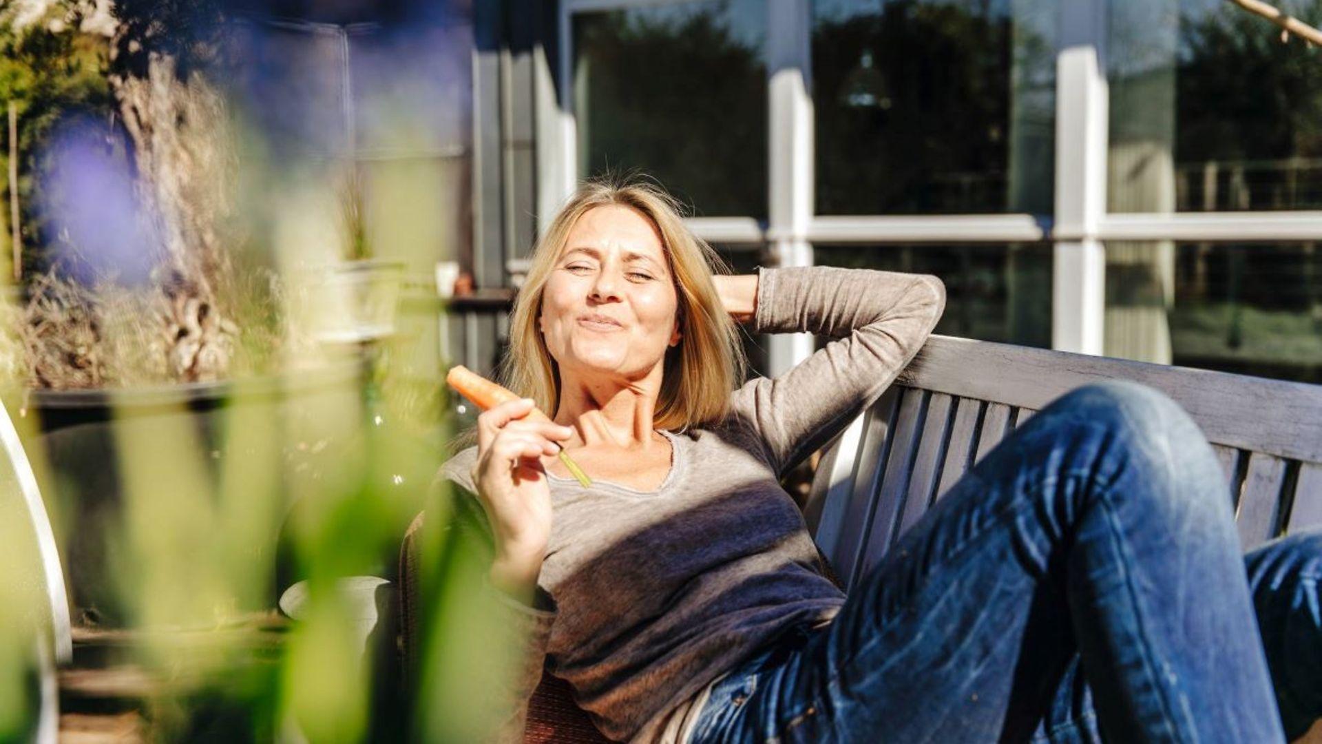 Frau relaxt auf einer Gartenliege und genießt die Sonnenstrahlen