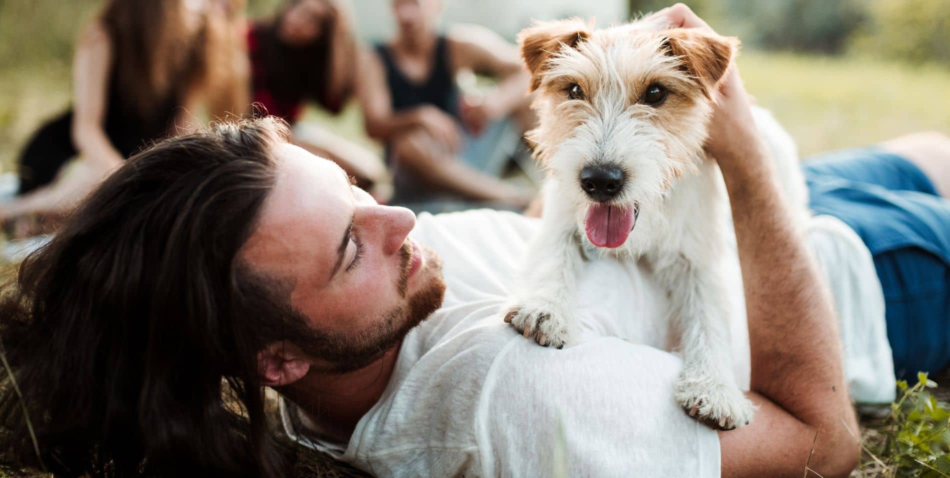 Mitglied bei der DAK-Gesundheit werden: Junger Mann entspannt mit seinem Hund im Park auf der Wiese.