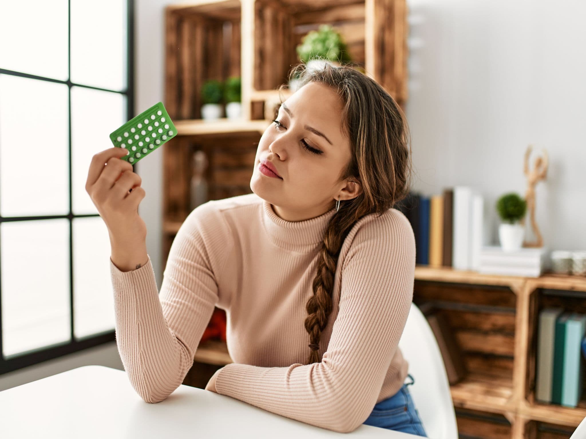 Pille absetzen: Eine Frau hält die Antibabypille in der Hand und denkt nach