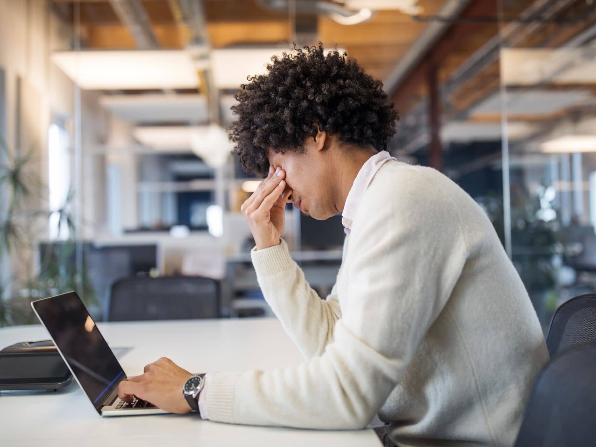 Person sitzt im Büro vor Laptop und hält sich nachdenklich die Stirn.